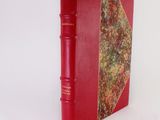 an old red book sitting on top of a table next to a white wall