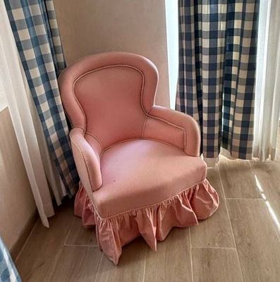 a pink chair sitting in front of a window next to a curtain