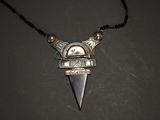 a close up of a necklace with a metal object on a black surface