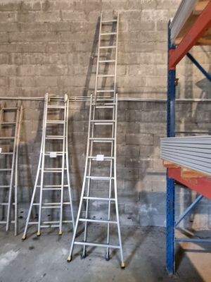 Plusieurs échelles sont alignées contre un mur dans un entrepôt.