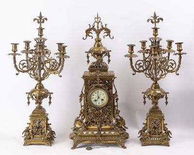 trois bougeoirs en laiton vieilli et une horloge sur fond blanc