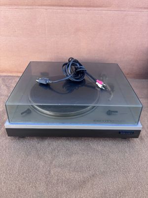 un gros plan d'une platine posée sur une surface recouverte de moquette, avec un cordon d'alimentation