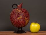 a red vase and an apple on a wooden table