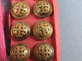 six gold buttons in a pink box on a table