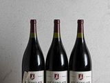 three bottles of wine sit on a wooden table in front of a wall