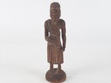 une vieille statue en bois représentant une personne debout sur une surface blanche
