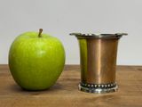 a green apple next to a silver cup on a wooden table