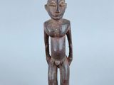 une vieille statue en bois représentant un homme debout, les mains dans les poches