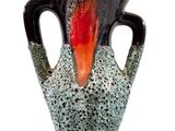 un vase noir et orange posé sur une surface blanche