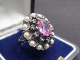 une photo d'une bague dans un écrin, avec des perles et une pierre rose