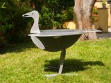 a metal duck sitting on top of a grill in the grass
