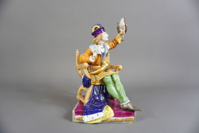 une figurine représentant un homme assis sur une chaise, tenant un oiseau dans la main