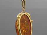 a close up of a gold plated pendant with an orange stone