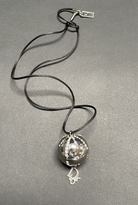 a close up of a necklace with a silver ball on a black cord