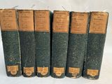 six old books are lined up in a row on a white surface