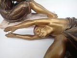 a bronze statue of a woman laying on a marble slab