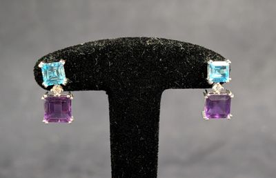 une paire de boucles d'oreilles en cristal violet et bleu, posées sur un socle noir