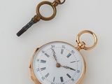 une montre de poche en or et une clé posées sur une table blanche