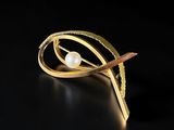 a close up of a gold brooch with a pearl in it