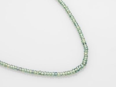 un gros plan d'un collier de perles vertes posé sur une surface blanche