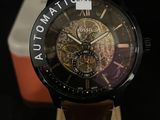 La montre est posée sur un socle en bois, avec une boîte en arrière-plan.