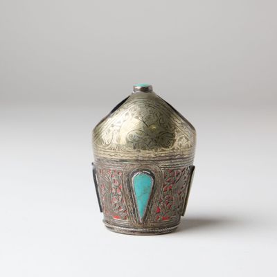 an old silver and turquoise vase sitting on top of a white surface