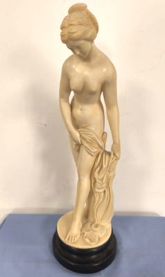 une statue blanche représentant une femme tenant une fleur, posée sur un fond bleu