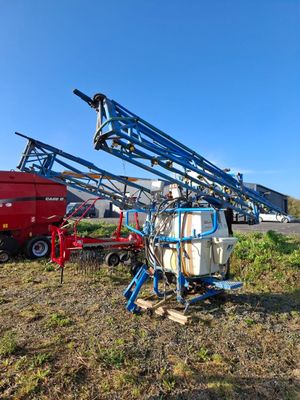 une grue bleue perchée au-dessus d'un champ, à côté d'un camion rouge