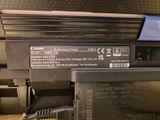 une imprimante Canon posée sur une table, avec un chargeur branché dessus