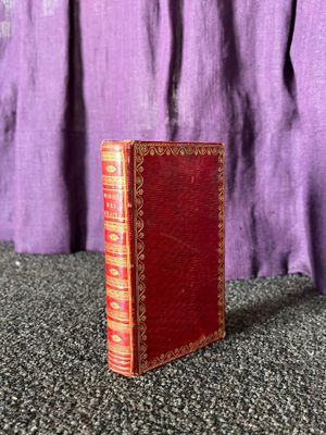 un vieux livre rouge posé sur une table, à côté d'un rideau violet