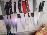 de nombreux couteaux accrochés au mur à côté d'une bouteille de vin