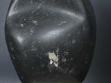 a black stone sculpture on a wooden stand against a gray background