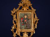 un cadre doré richement décoré, dans lequel est accrochée une peinture représentant un homme assis sur une chaise rouge