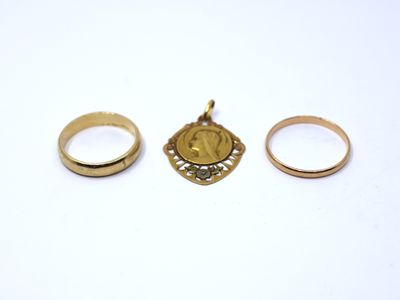 two gold rings and a gold pendant on a white surface