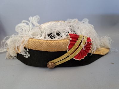 un chapeau noir orné de passementerie dorée et d'un ruban rouge