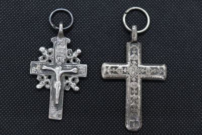 two silver cross charms on a black background