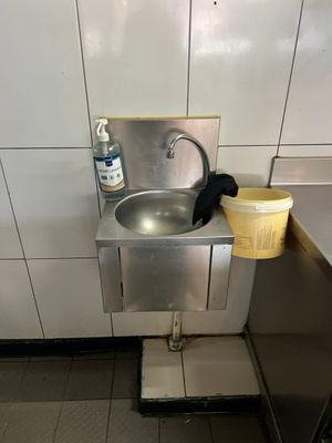 un lavabo dans des toilettes publiques, avec un seau posé par terre