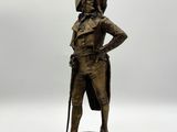 Une statue représentant un homme coiffé d'un chapeau et muni d'une canne se dresse sur une surface blanche