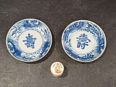 two blue and white plates with chinese writing on them next to a small container