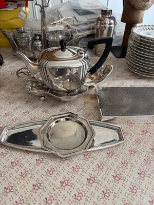 une théière en argent posée sur une table, à côté d'autres théières en argent