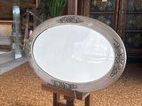 a large oval mirror on a stand in the middle of a room