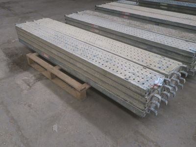 Plusieurs pièces métalliques sont empilées sur des palettes dans un entrepôt