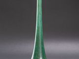 green glass vase on a gray surface with a shadow on the ground