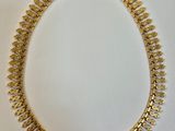 un collier en or posé sur une surface blanche, sur fond blanc