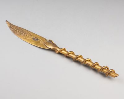 un couteau plaqué or avec un manche en forme de feuille posé sur une surface blanche