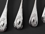four silver spoons with ornate designs are lined up on a black surface