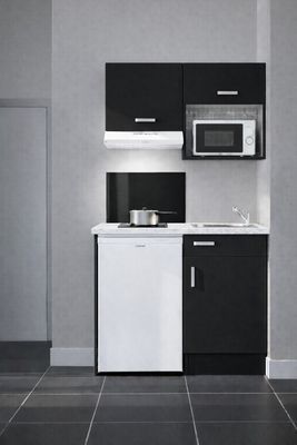 une petite cuisine avec des placards noirs et blancs et un réfrigérateur blanc