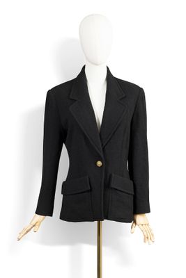 une veste noire posée sur un mannequin, sur une surface blanche