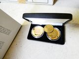 two gold coins in a black box next to an open book