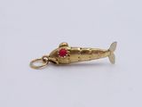 an image of a gold fish charm with a red bead on it